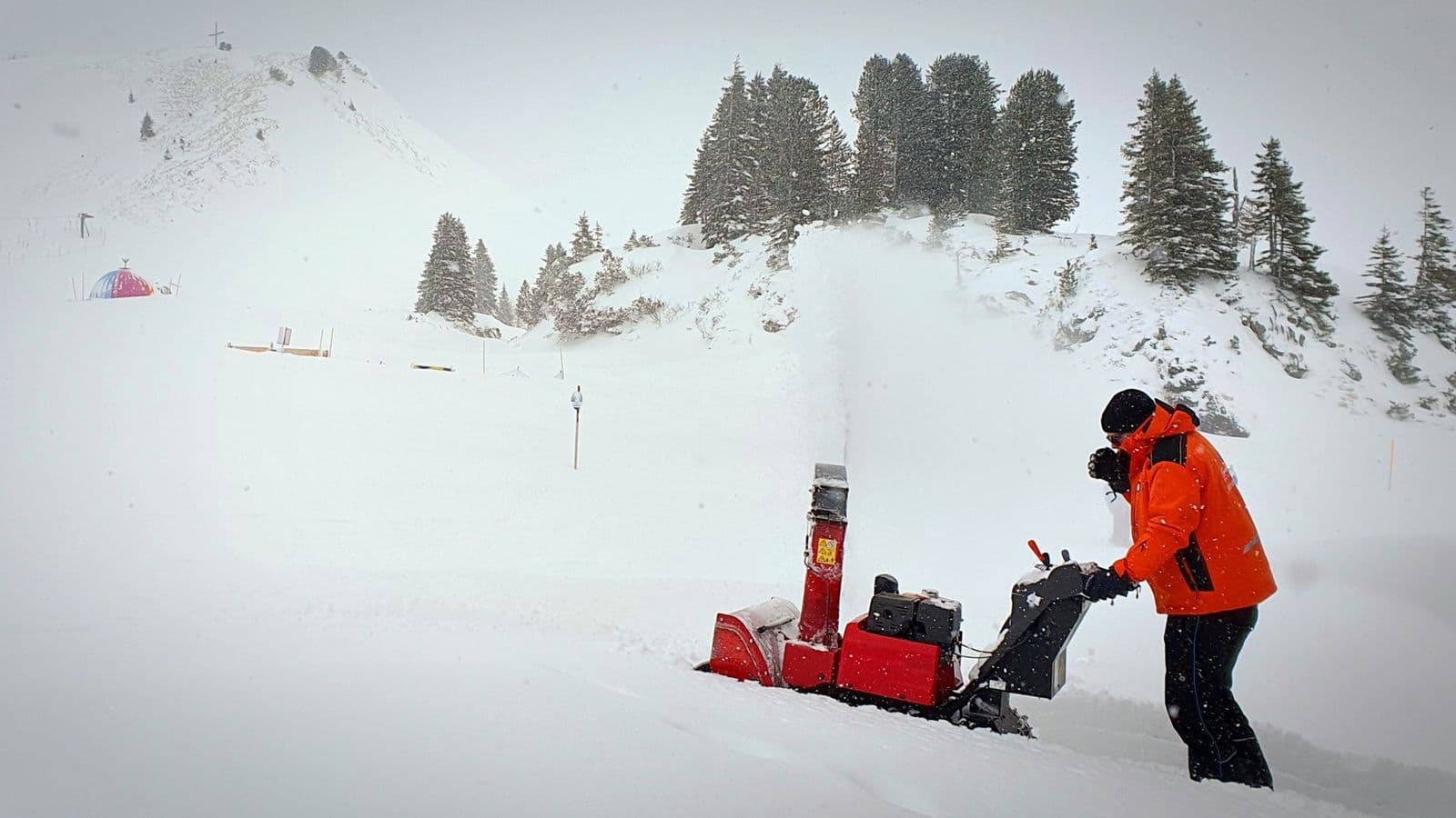 Man in an orange jacket running a snowblower in winter, a reminder of how long does a snow blower last with care
